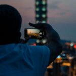 A man capturing a city skyline with his smartphone during dusk, highlighting urban photography.