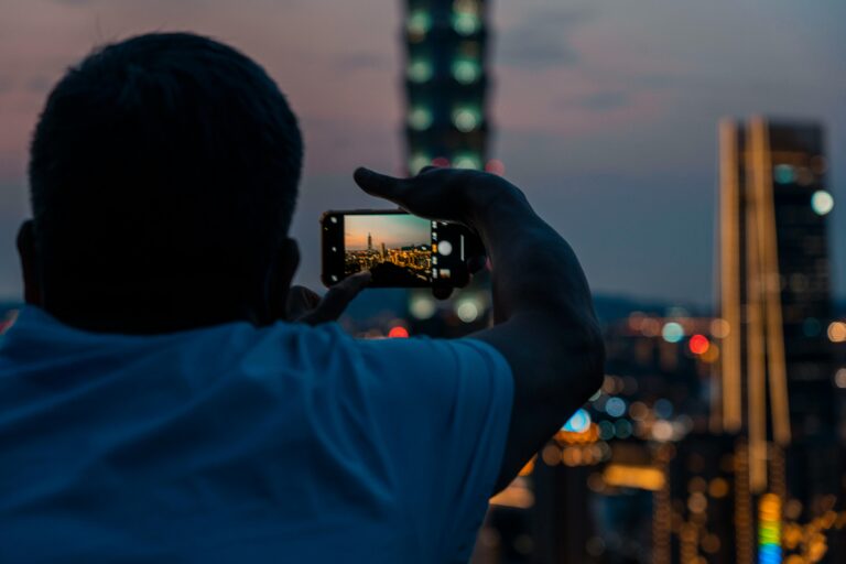 A man capturing a city skyline with his smartphone during dusk, highlighting urban photography.