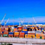 A bustling shipping port with colorful stacked containers and numerous cranes under a clear blue sky.