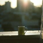 A mug sits on a windowsill with the city skyline and sunrise in the background.