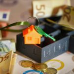 Image depicting real estate investment with keychain, euros, and financial charts.