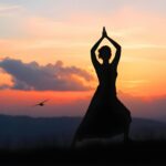 Silhouette of a woman practicing yoga during a serene sunset outdoors.