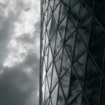 Dark glass facade reflects swirling clouds, creating a dramatic and abstract architectural view.