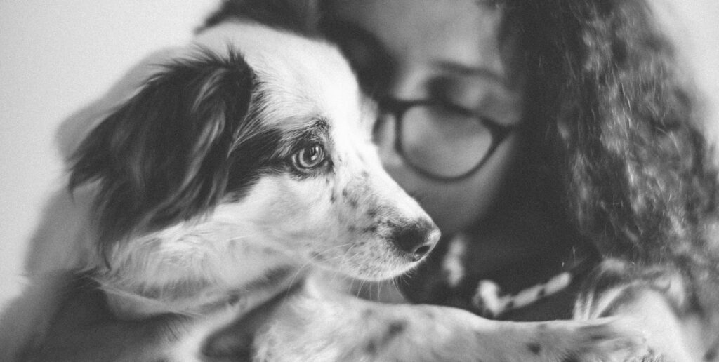 A touching black and white portrait of a girl lovingly hugging her dog.