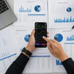 Business person reviews financial data and graphs on a mobile device surrounded by reports.