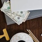Stylish workspace featuring coffee cup, dollar bills, laptop, and stationery on a wooden table.
