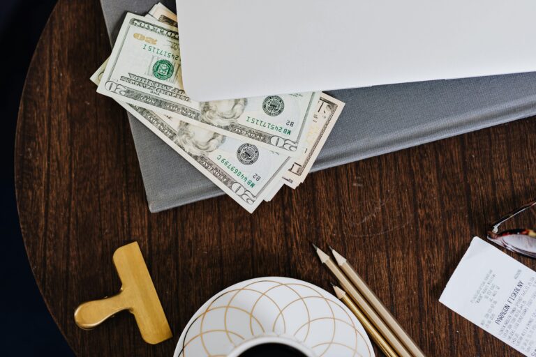 Stylish workspace featuring coffee cup, dollar bills, laptop, and stationery on a wooden table.