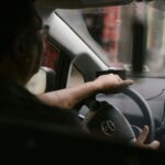 Back view of crop anonymous man in eyeglasses driving car in rainy day
