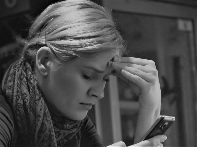 Black and white image of a woman deep in thought, holding a smartphone indoors.