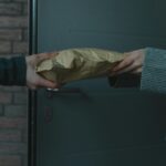 Close-up of hands exchanging a package at a doorway, symbolizing home delivery service.