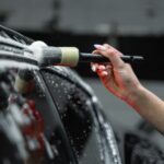 Hand cleaning car exterior with brush and foam in a detailed car wash process.