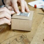 Close-up of hands packing a box with a QR code, symbolizing online business services.
