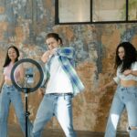Group of friends dancing indoors with a smartphone and ring light setup for social media content.