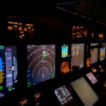 A focused view of an aircraft cockpit control panel with various illuminated screens.