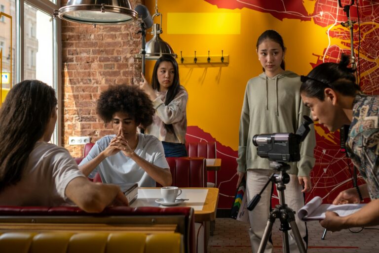 Film crew capturing a scene in a lively cafe setting with diverse actors and a cameraman.