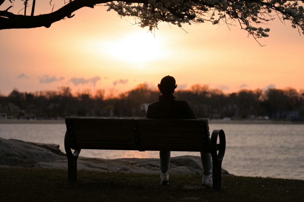 A person reflects quietly on a bench by the water at sunrise in Cove Island Park, Stamford.