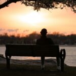 A person reflects quietly on a bench by the water at sunrise in Cove Island Park, Stamford.