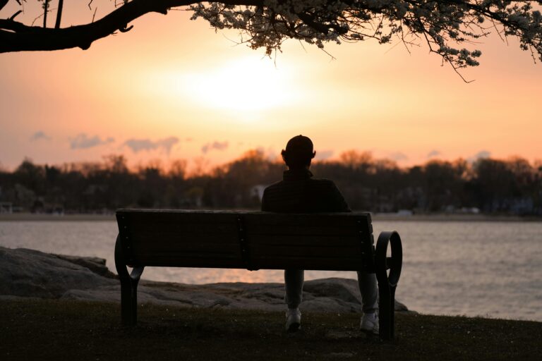 A person reflects quietly on a bench by the water at sunrise in Cove Island Park, Stamford.