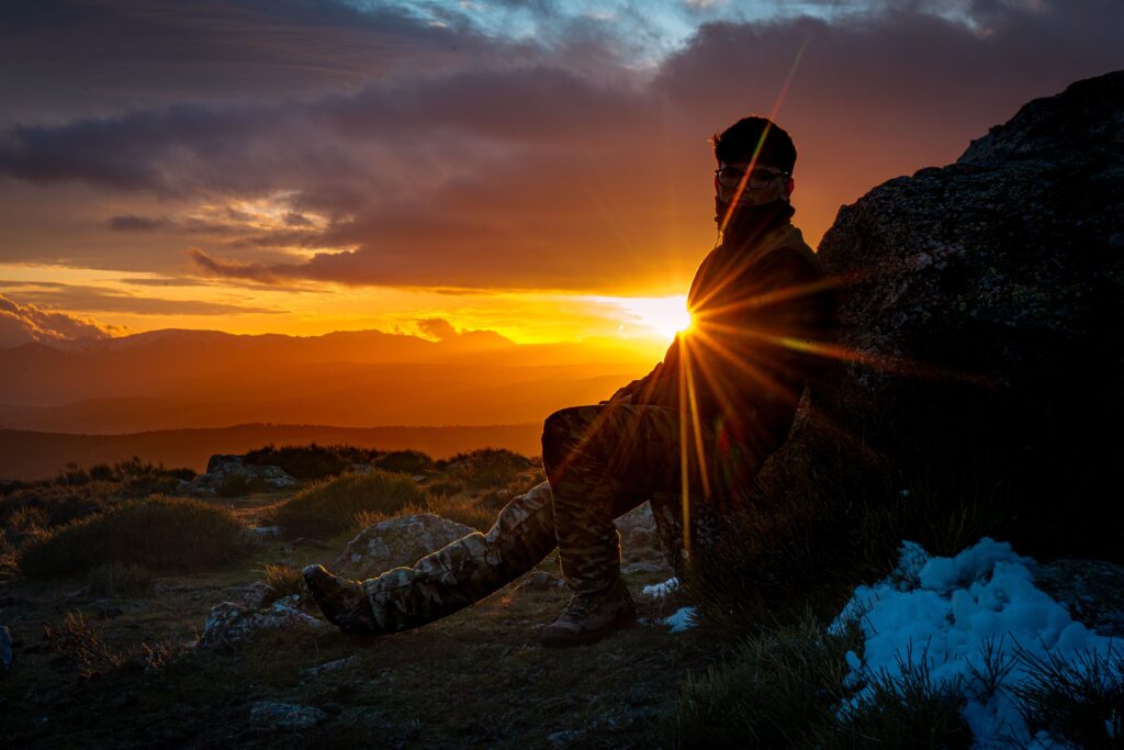 A person sits on a mountain rock at sunset, creating a stunning silhouette against the vibrant sky.
