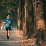An athletic man runs along a picturesque tree-lined street during autumn. Perfect for fitness and outdoor themes.