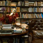 A vintage study room featuring a leather armchair, bookshelves, and a rustic table with decor.