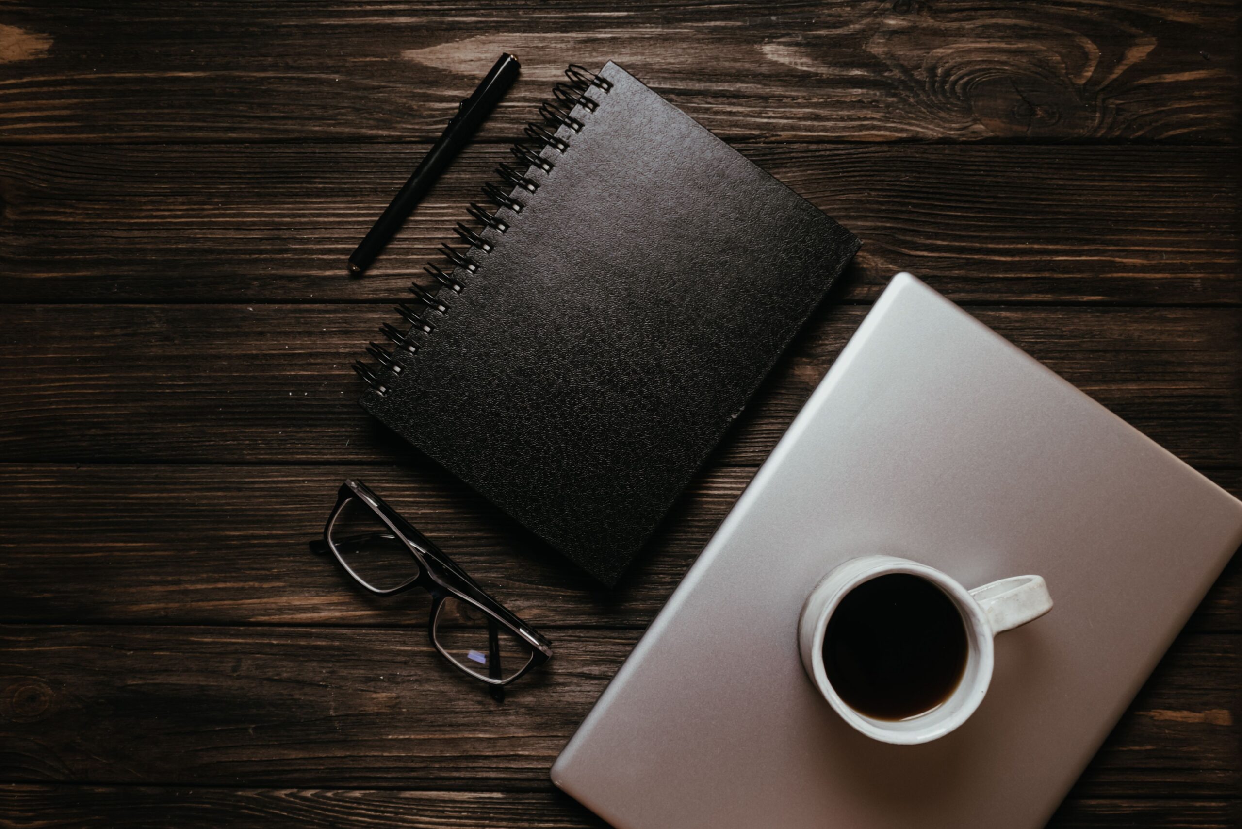 Top view of a wooden desk with a cup of coffee, notebook, pen, and laptop, perfect for productivity.