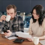 A couple reviewing bills, using a calculator and smartphone, in a modern kitchen.