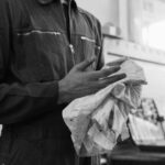 Mechanic cleaning hands with cloth in a monochrome automotive workshop setting.