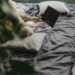 Relaxed work environment with a laptop and person typing on a bed, enjoying comfort while working.
