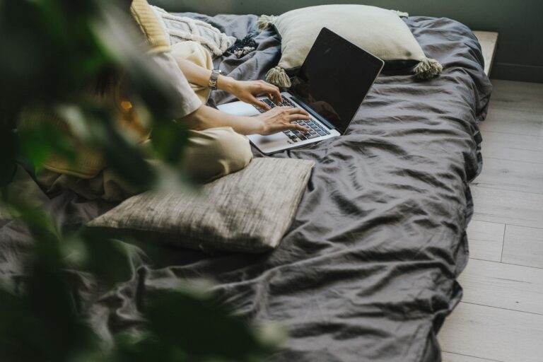 Relaxed work environment with a laptop and person typing on a bed, enjoying comfort while working.